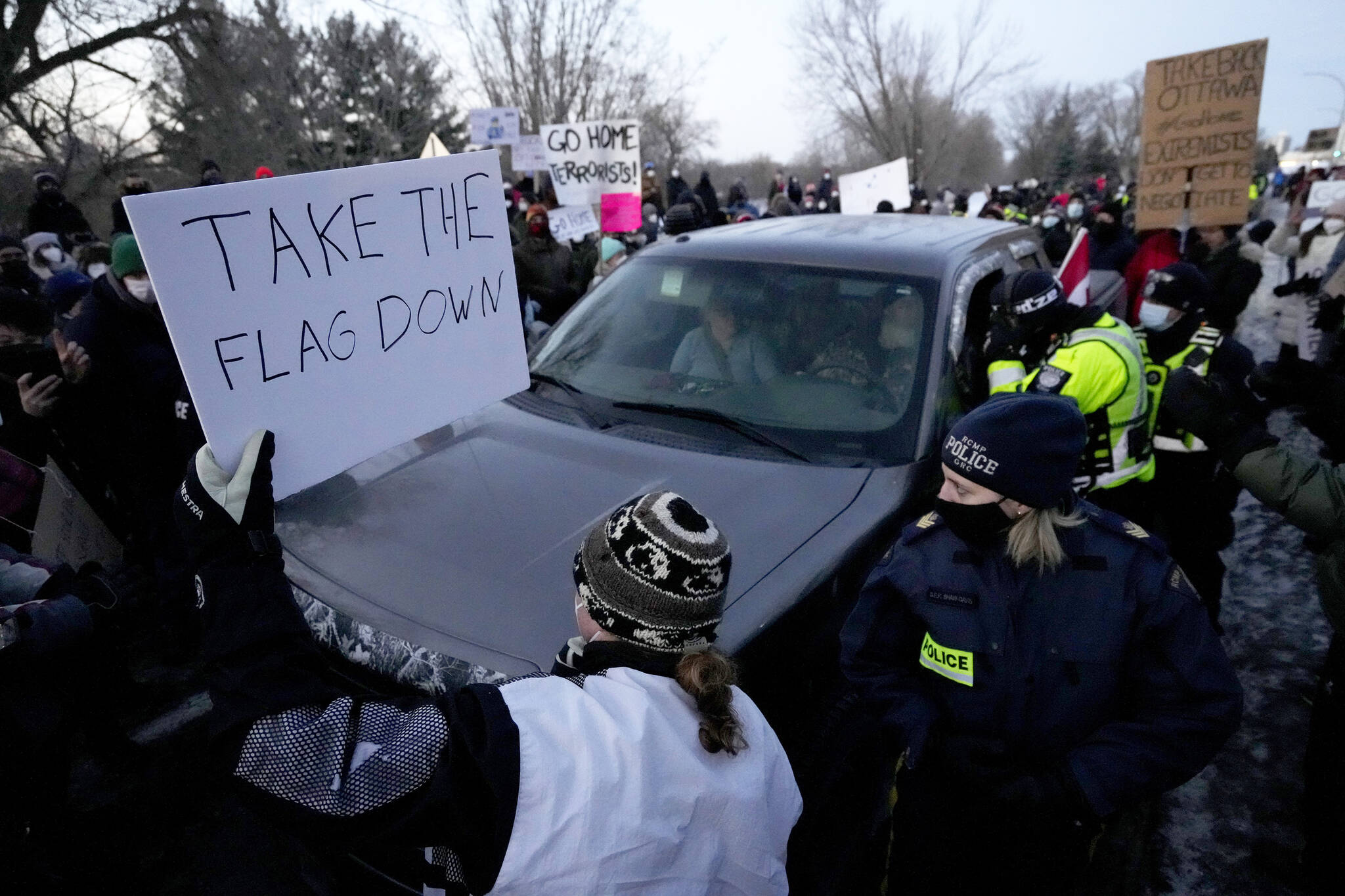 A resident holds a sign calling for a convoy participant to remove their Canadian flag as they negotiate to release vehicles from a counter protest that blocked Riverside Drive for hours, in Ottawa, Sunday, Feb. 13, 2022. The protest, which began as a cross country convoy against COVID-19 measures but has manifested into a broader anti-government protest, has been marked by the sound of truck horns and the waving of the Canadian flag, sometimes upside down, which residents argued was a co-opting of the flag. THE CANADIAN PRESS/Justin Tang