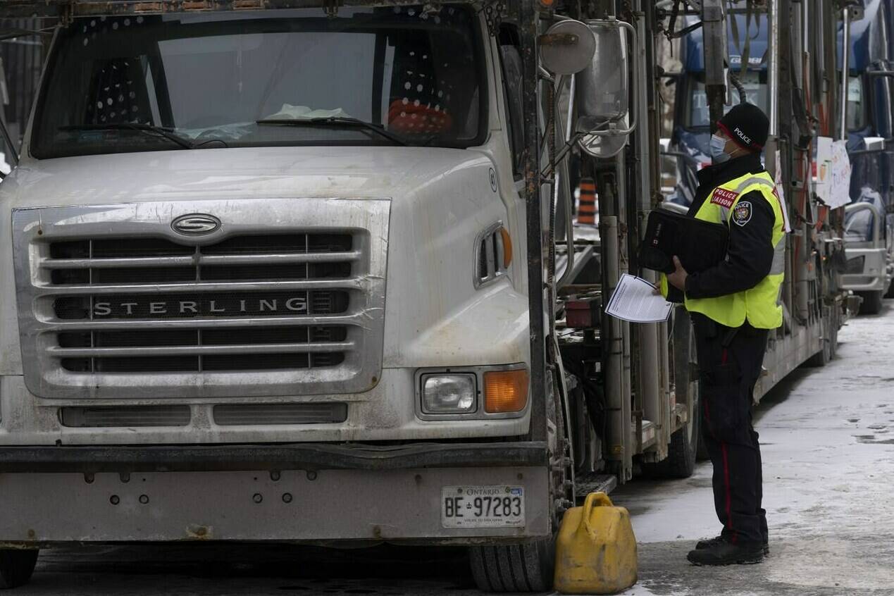 A police officer speaks with a trucker as he distributes a notice to protesters, Wednesday, Feb. 16, 2022 in Ottawa. THE CANADIAN PRESS/Adrian Wyld