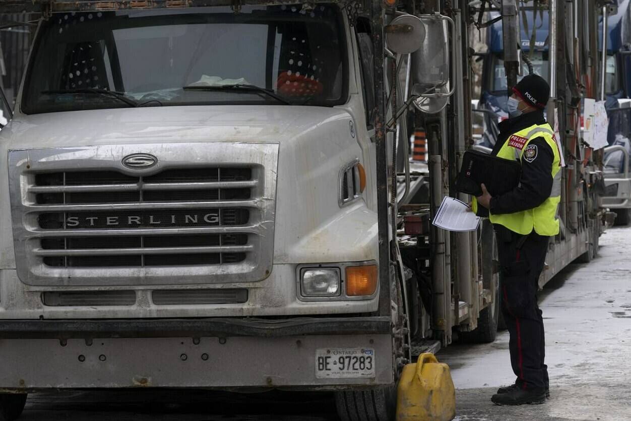A police officer speaks with a trucker as he distributes a notice to protesters, Wednesday, Feb. 16, 2022 in Ottawa. THE CANADIAN PRESS/Adrian Wyld