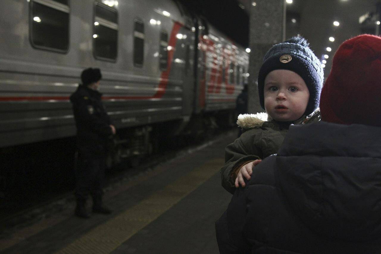 A woman carries a child as they are evacuated from the Donetsk region, the territory controlled by pro-Russia separatist government in eastern Ukraine, as they leave a train to be taken to temporary accommodations, at the railway station in Nizhny Novgorod, Russia, Tuesday, Feb. 22, 2022. A long-feared Russian invasion of Ukraine appears to be imminent, if not already underway, with Russian President Vladimir Putin ordering forces into separatist regions of eastern Ukraine. (AP Photo/Roman Yarovitcyn)