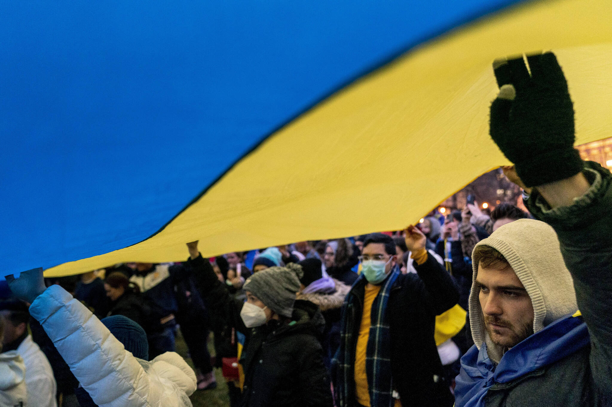 People stand under a giant Ukrainian flag during a vigil to protest the Russian invasion of Ukraine in front of the White House in Washington, Thursday, Feb. 24, 2022. (AP Photo/Andrew Harnik)