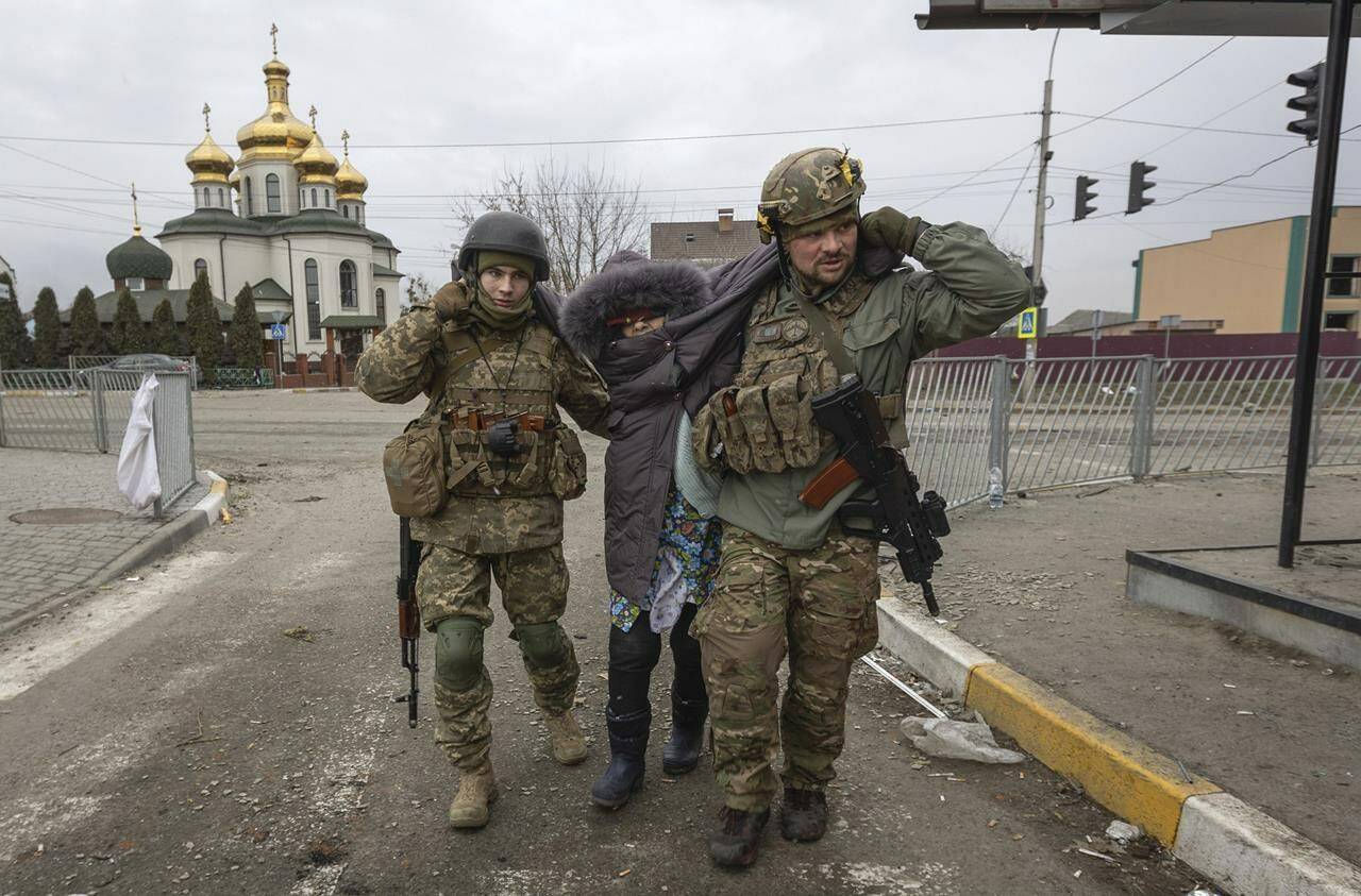 Ukrainian servicemen help an elderly woman, in the town of Irpin, Ukraine, Sunday, March 6, 2022. With the Kremlin’s rhetoric growing fiercer and a reprieve from fighting dissolving, Russian troops continued to shell encircled cities and the number of Ukrainians forced from their country grew to over 1.4 million. (AP Photo/Andriy Dubchak)