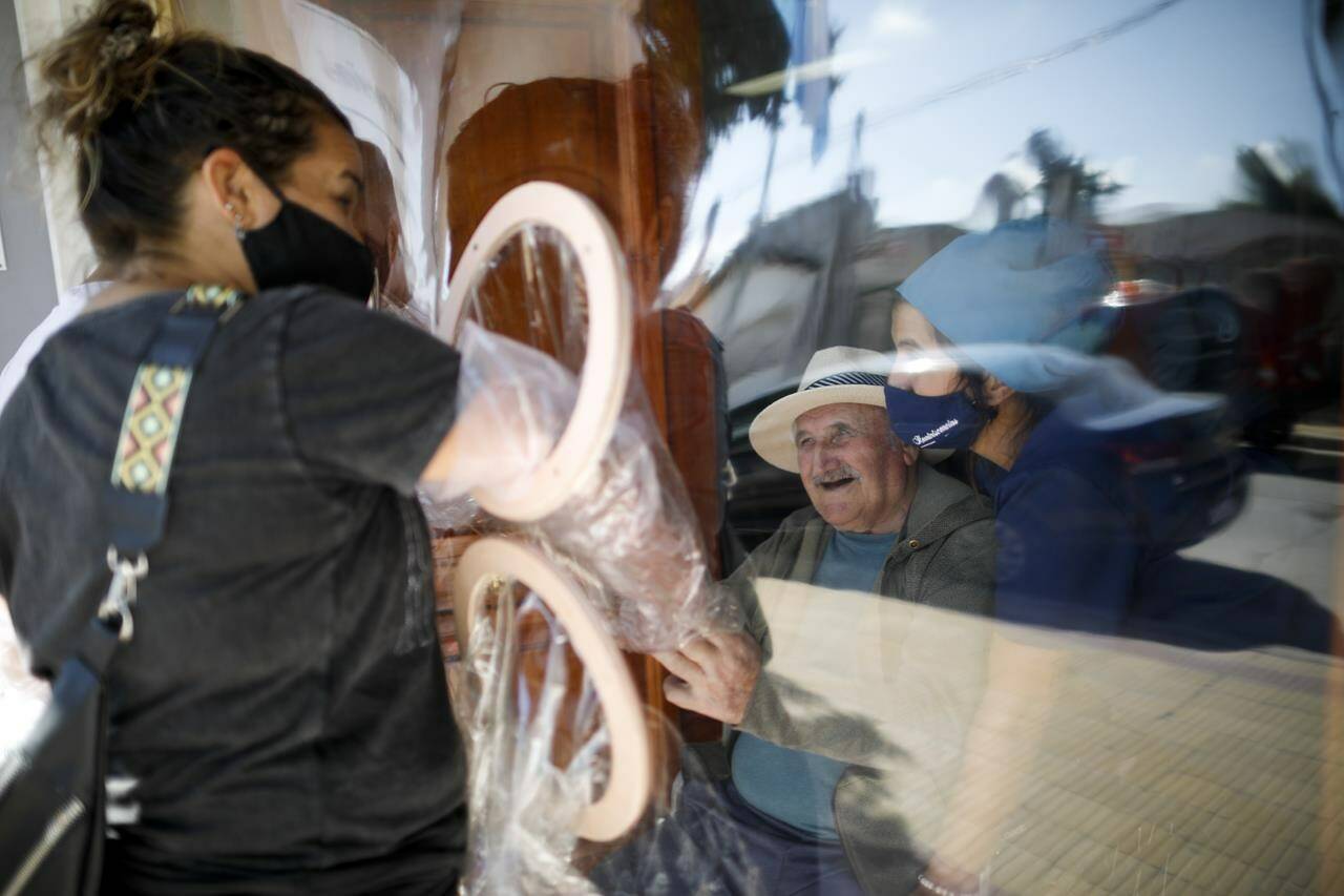 Debora Aberastegui holds the hands of her father Pedro Aberastegui through a plastic sleeve at the Reminiscencias residence for the elderly in Tandil, Argentina, Monday, April 5, 2021. Residents here do not have physical contact with their families or leave the residence due to the COVID-19 pandemic, but stay active with group activities within the facility. (AP Photo/Natacha Pisarenko)