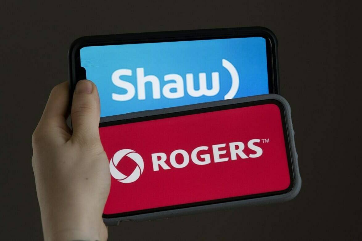 A woman holds two cellphones in this photo illustration, Monday March 29, 2021 in Chelsea, Que. The CRTC has approved Rogers’ acquisition of Shaw’s broadcasting services, subject to some conditions and modifications. THE CANADIAN PRESS/Adrian Wyld