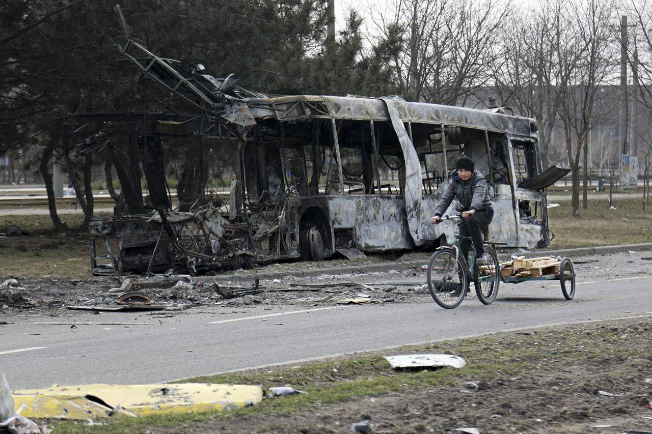 A woman rides a bicycle past a burned bus after fighting on the outskirts of Mariupol, Ukraine, in territory under control of the separatist government of the Donetsk People’s Republic, on Tuesday, March 29, 2022. International Development Minister Harjit Sajjan and Public Safety Minister Marco Mendicino discuss the International Criminal Court investigation into alleged war crimes by Russia. (AP Photo/Alexei Alexandrov)