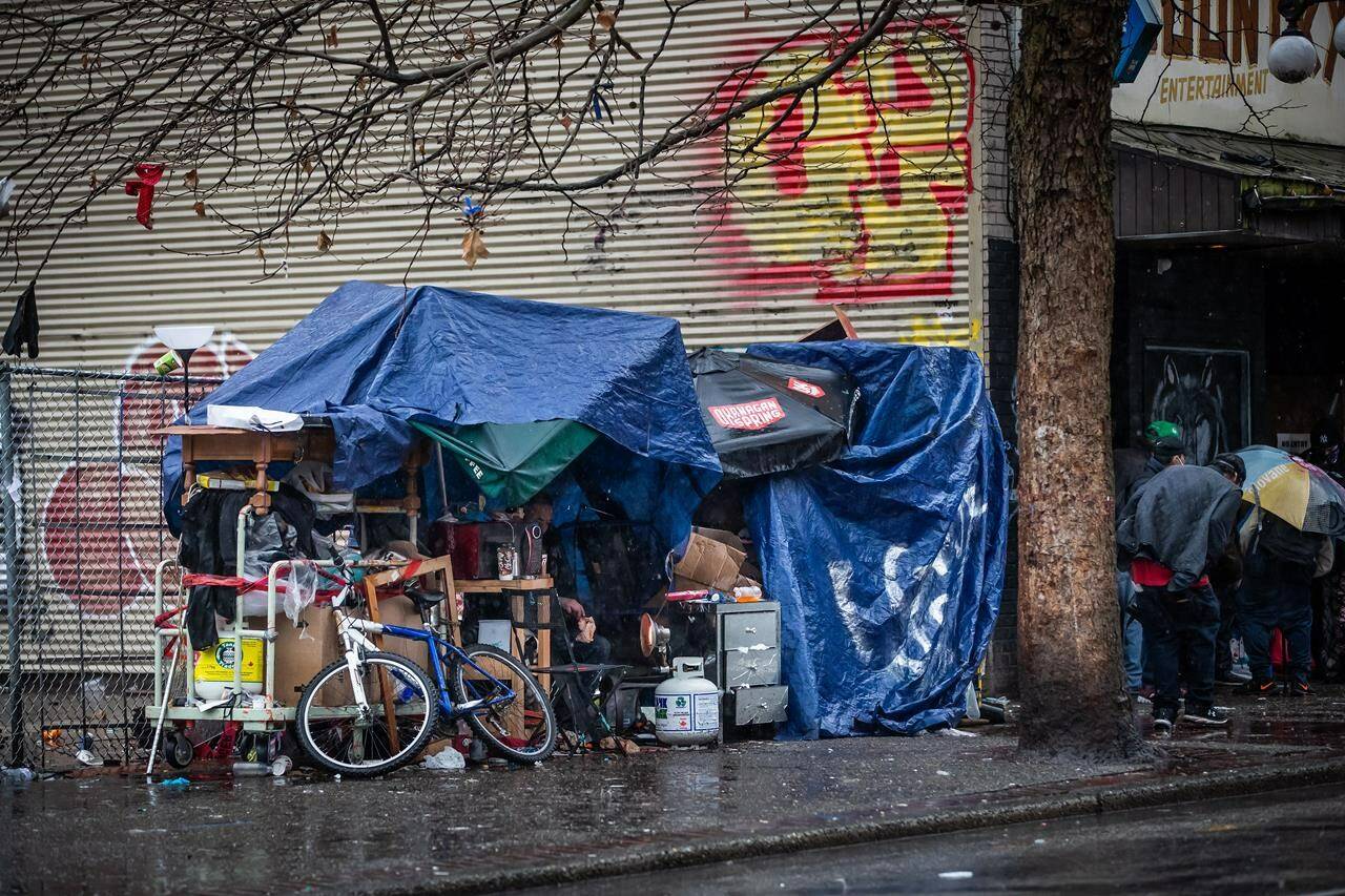 A homeless person uses a portable propane heater to try and stay warm under umbrellas and tarps as rain falls in the Downtown Eastside of Vancouver, on Sunday, December 13, 2020. THE CANADIAN PRESS/Darryl Dyck