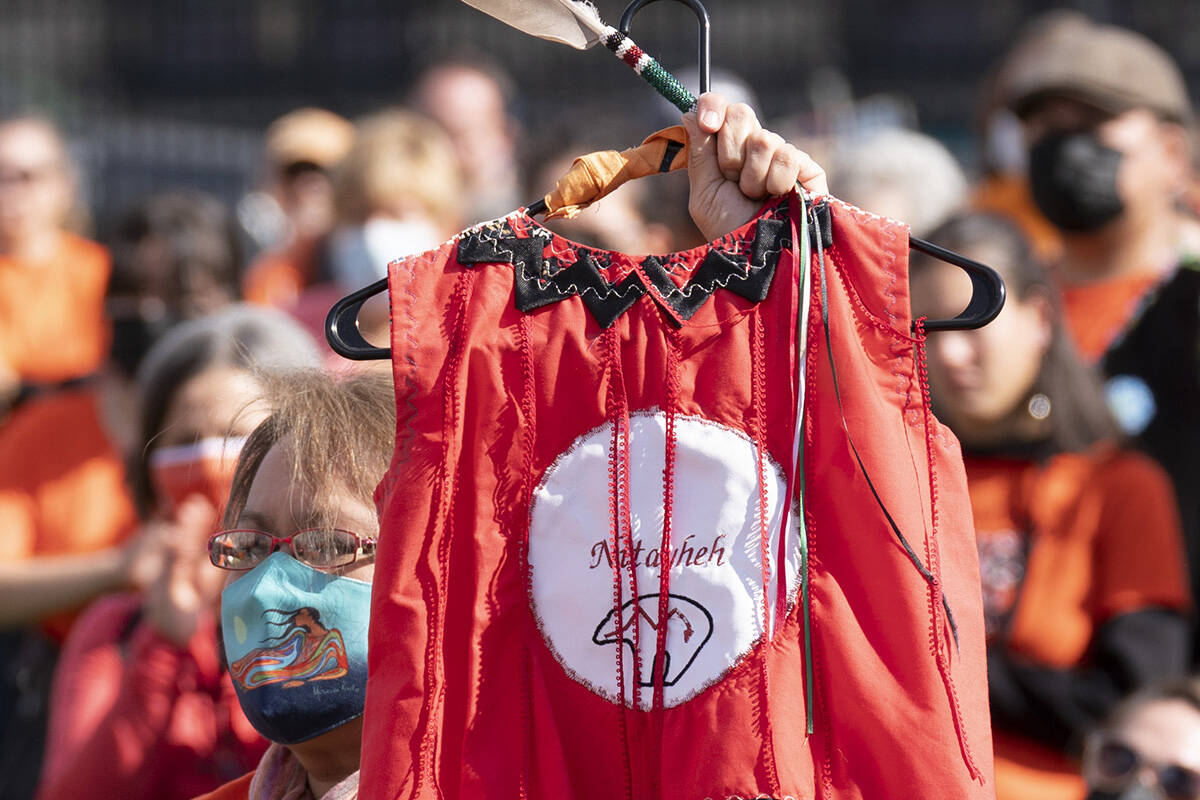 A woman holds an eagle feather and red dress as she listens to speakers during National Day of Truth and Reconciliation ceremonies on Parliament Hill September 30, 2021 in Ottawa. Red dresses have become a symbol for missing and murdered Indigenous women and girls in Canada. THE CANADIAN PRESS/Adrian Wyld