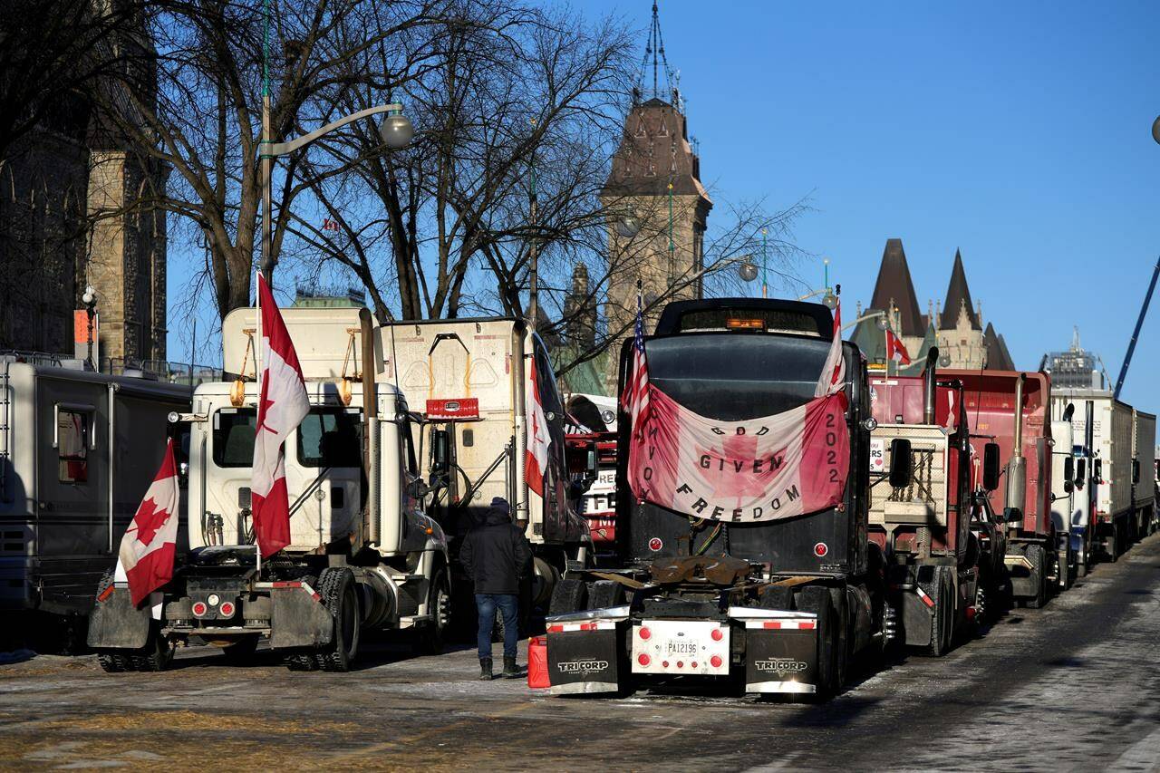 A person walks among trucks as Wellington Street is lined with trucks on the 18th day of a protest against COVID-19 measures that has grown into a broader anti-government protest, in Ottawa, on Monday, Feb. 14, 2022. Ottawa convoy protest organizer Pat King is now facing perjury and obstruction of justice charges as he tries to secure his release from jail. THE CANADIAN PRESS/Justin Tang