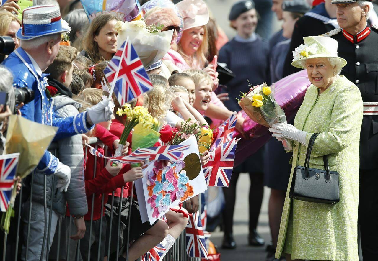 FILE - Britain’s Queen Elizabeth II collects flowers and good wishes during a walkabout to celebrates her 90th birthday in Windsor, England, Thursday, April, 21, 2016. Queen Elizabeth II is marking her 96th birthday privately on Thursday, April 21, 2022, retreating to the Sandringham estate in eastern England that has offered the monarch and her late husband, Prince Philip, a refuge from the affairs of state. (AP Photo/Alastair Grant, File)