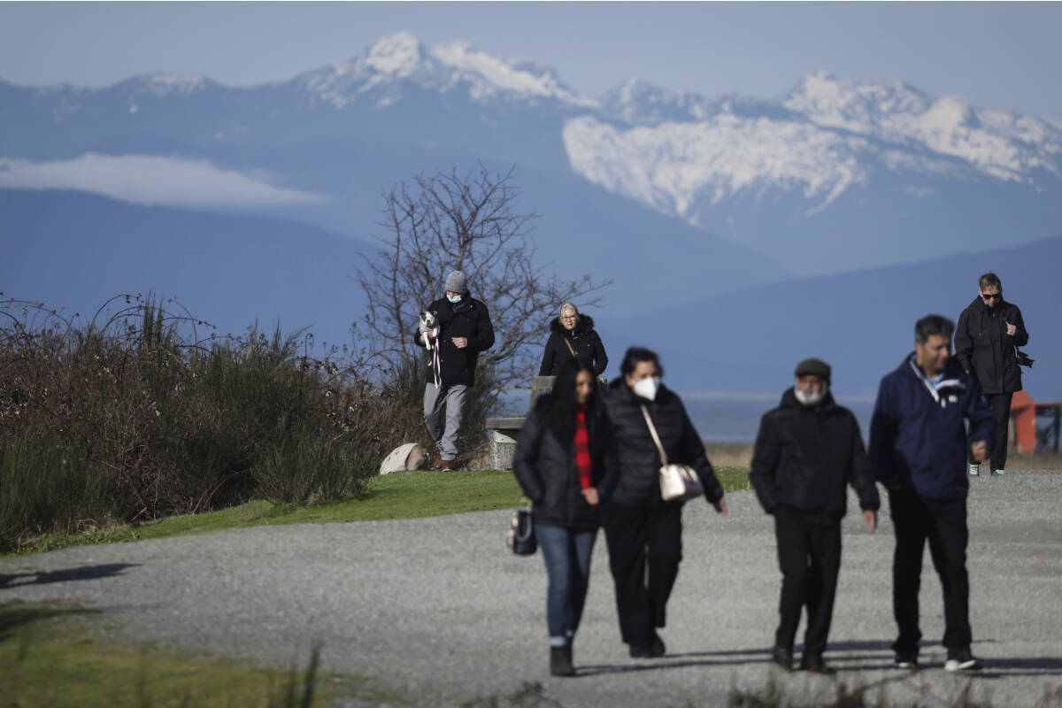 A man wearing a face mask to curb the spread of COVID-19 carries a dog as he and others walk on a trail at Garry Point Park, in Richmond, B.C., on Saturday, January 22, 2022. THE CANADIAN PRESS/Darryl Dyck