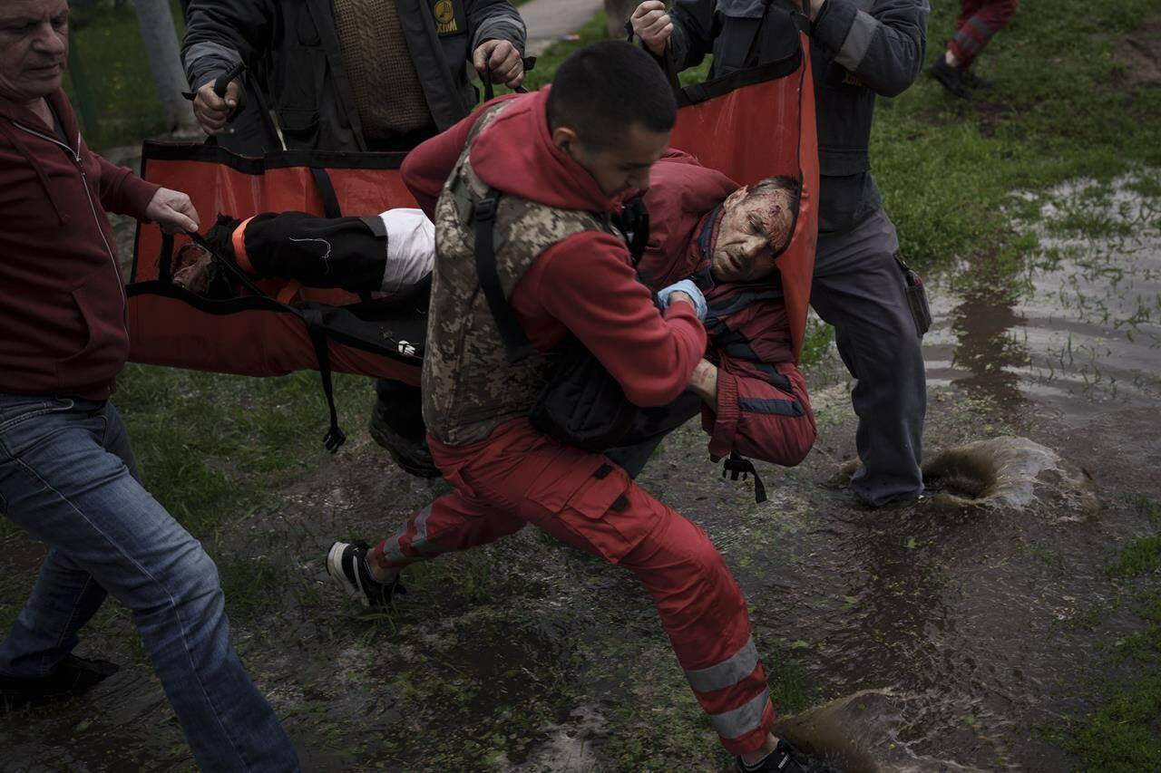 An emergency worker is helped by locals to carry a man to an ambulance following a Russian bombardment in Kharkiv, Ukraine, Wednesday, April 27, 2022. (AP Photo/Felipe Dana)