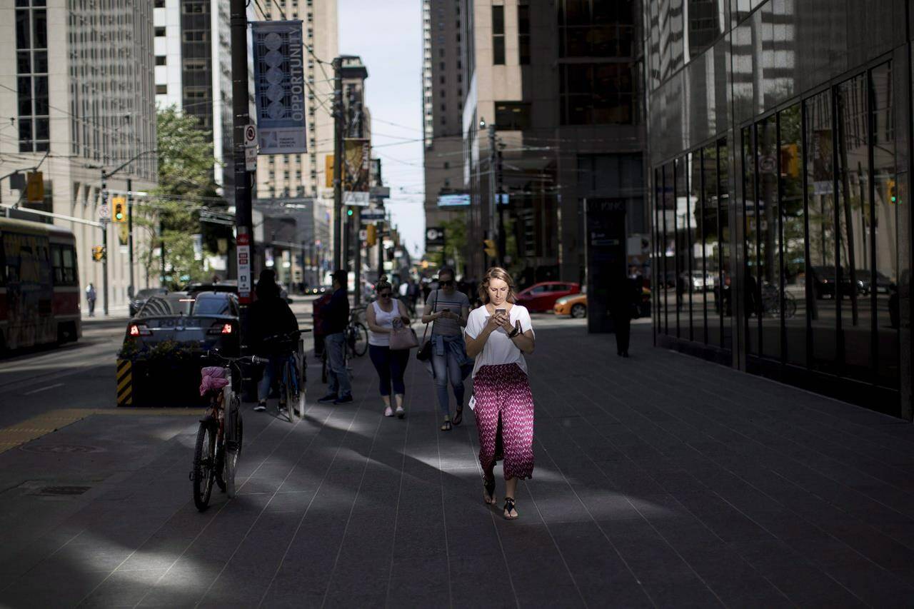 A woman looks down at her cell phone while walking though downtown Toronto, on Tuesday, June 12, 2018. A House of Commons committee says the federal government needs to tell Canadians if it’s collecting data about their movements, and allow them to opt out of that collection. THE CANADIAN PRESS/Chris Young