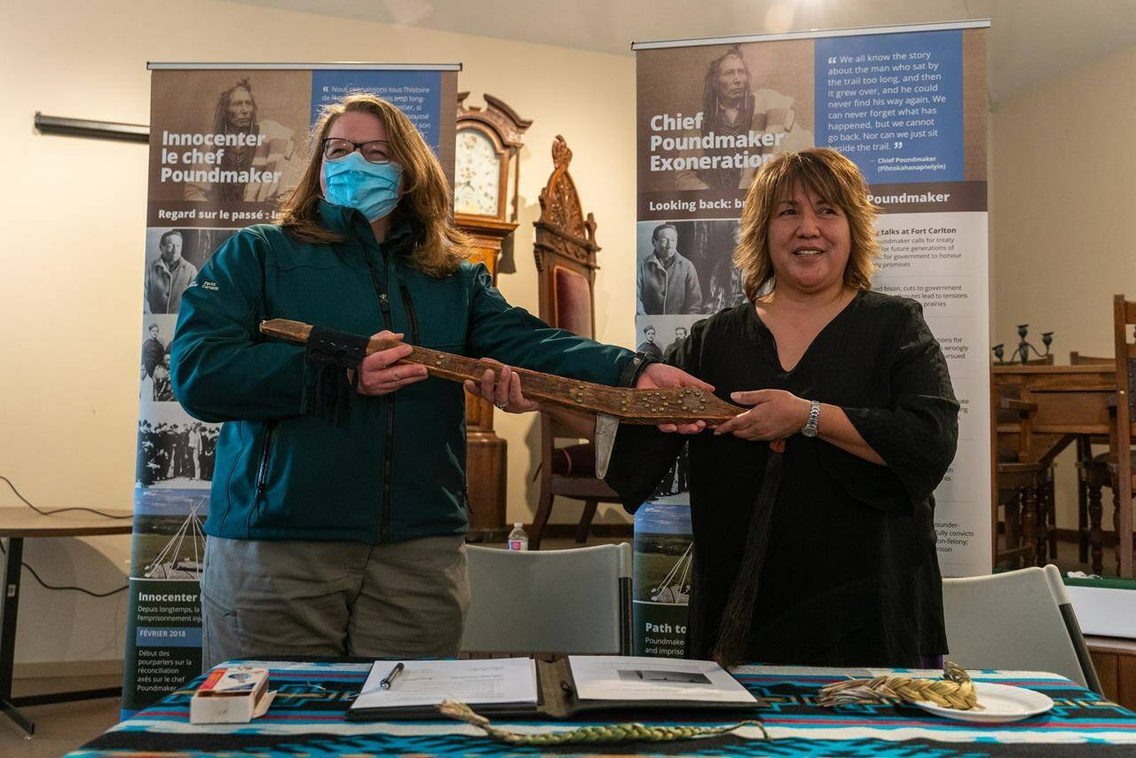 Parks Canada representative Genevieve Jones, left, hands over Chief Poundmaker's staff to Pauline Poundmaker, his great-great-granddaughter, right, after signing a transfer agreement during a ceremony at Fort Battleford National Historic Site near Battleford, Sask., on Wednesday, May 4, 2022. THE CANADIAN PRESS/Heywood Yu