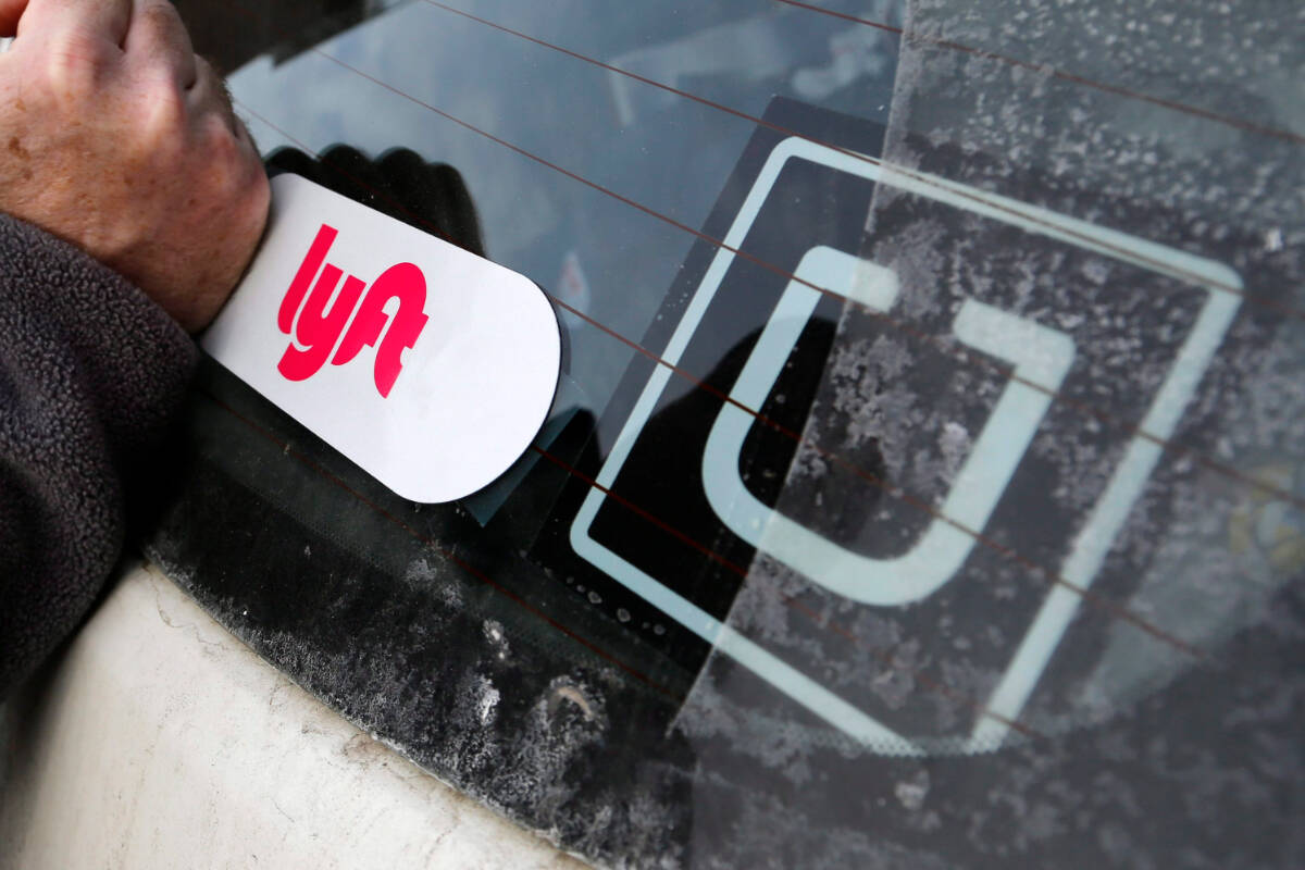 In this Jan. 31, 2018, file photo, a Lyft logo is installed on a Lyft driver’s car next to an Uber sticker. (AP Photo/Gene J. Puskar)