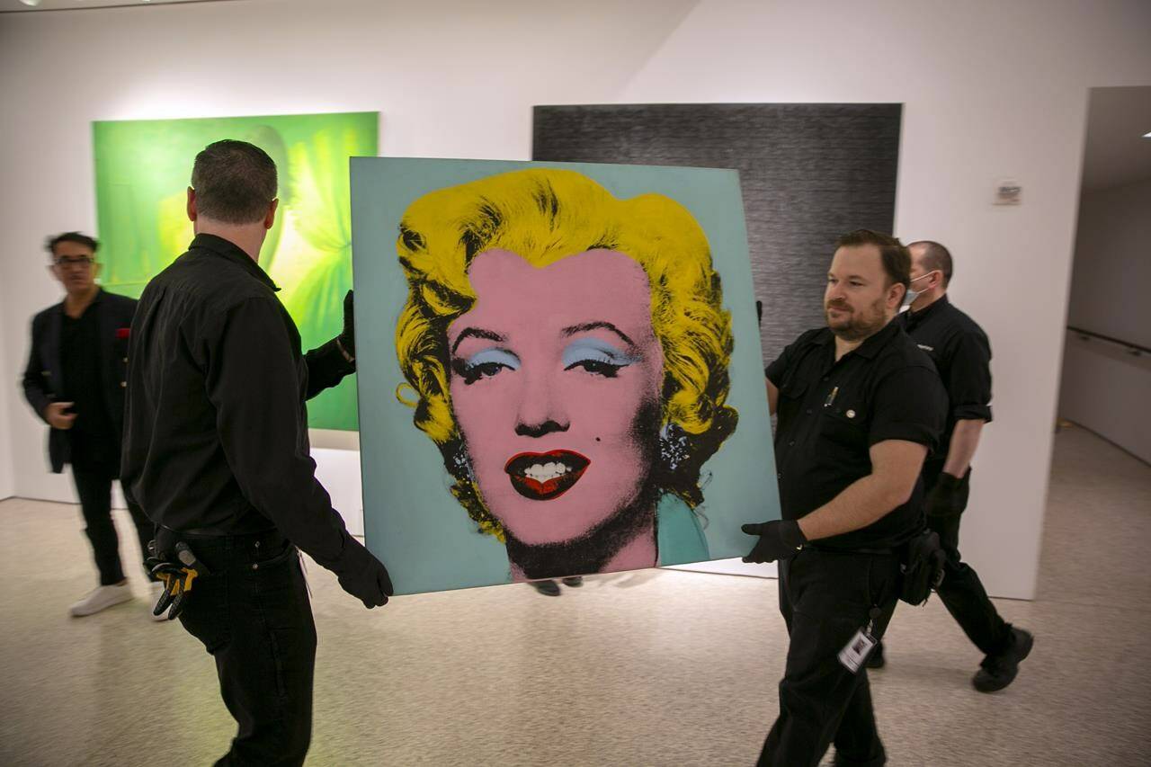 The 1964 painting Shot Sage Blue Marilyn by Andy Warhol is carried in Christie’s showroom in New York City on Sunday, May 8, 2022. The auction house predicts it will sell for $200 million on Monday, becoming the most expensive 20th-century artwork to sell at auction. (AP Photo/Ted Shaffrey)