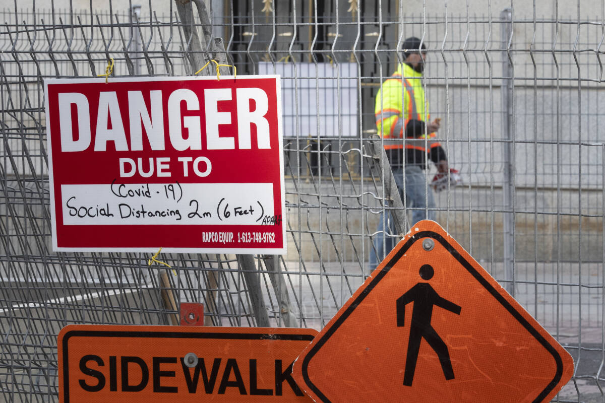 A construction sign on a fence surrounding an excavation indicates the danger is Covid-19 as a construction worker walks past. THE CANADIAN PRESS/Adrian Wyld