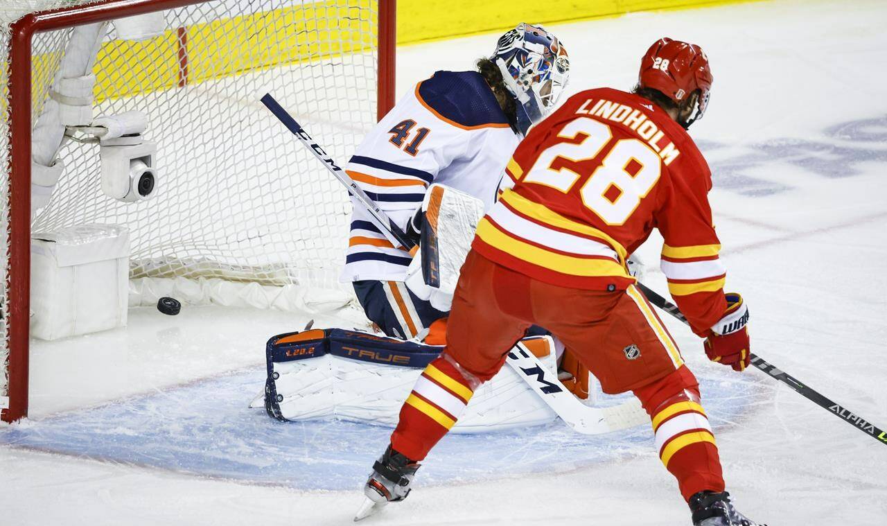 Edmonton Oilers goalie Mike Smith, left, lets in a goal as Calgary Flames forward Elias Lindholm looks on during first period NHL second round playoff hockey action in Calgary, Alta., Friday, May 20, 2022. THE CANADIAN PRESS/Jeff McIntosh