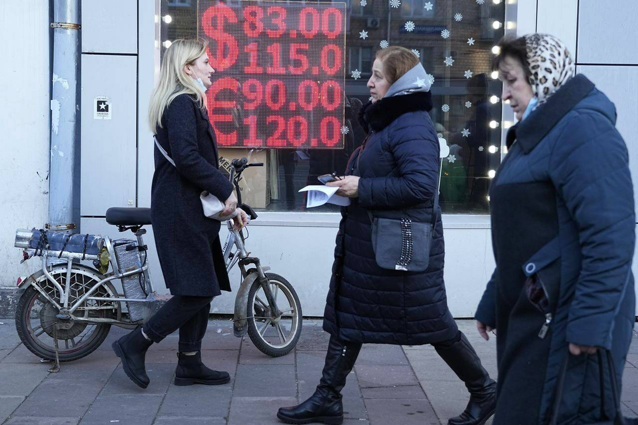FILE - People walk past a currency exchange office screen displaying the exchange rates of U.S. Dollar and Euro to Russian Rubles in Moscow’s downtown, Russia, Feb. 28, 2022. Ordinary Russians are facing the prospect of higher prices as Western sanctions over the invasion of Ukraine sent the ruble plummeting. That’s led uneasy people to line up at banks and ATMs on Monday in a country that has seen more than one currency disaster in the post-Soviet era. (AP Photo, File)