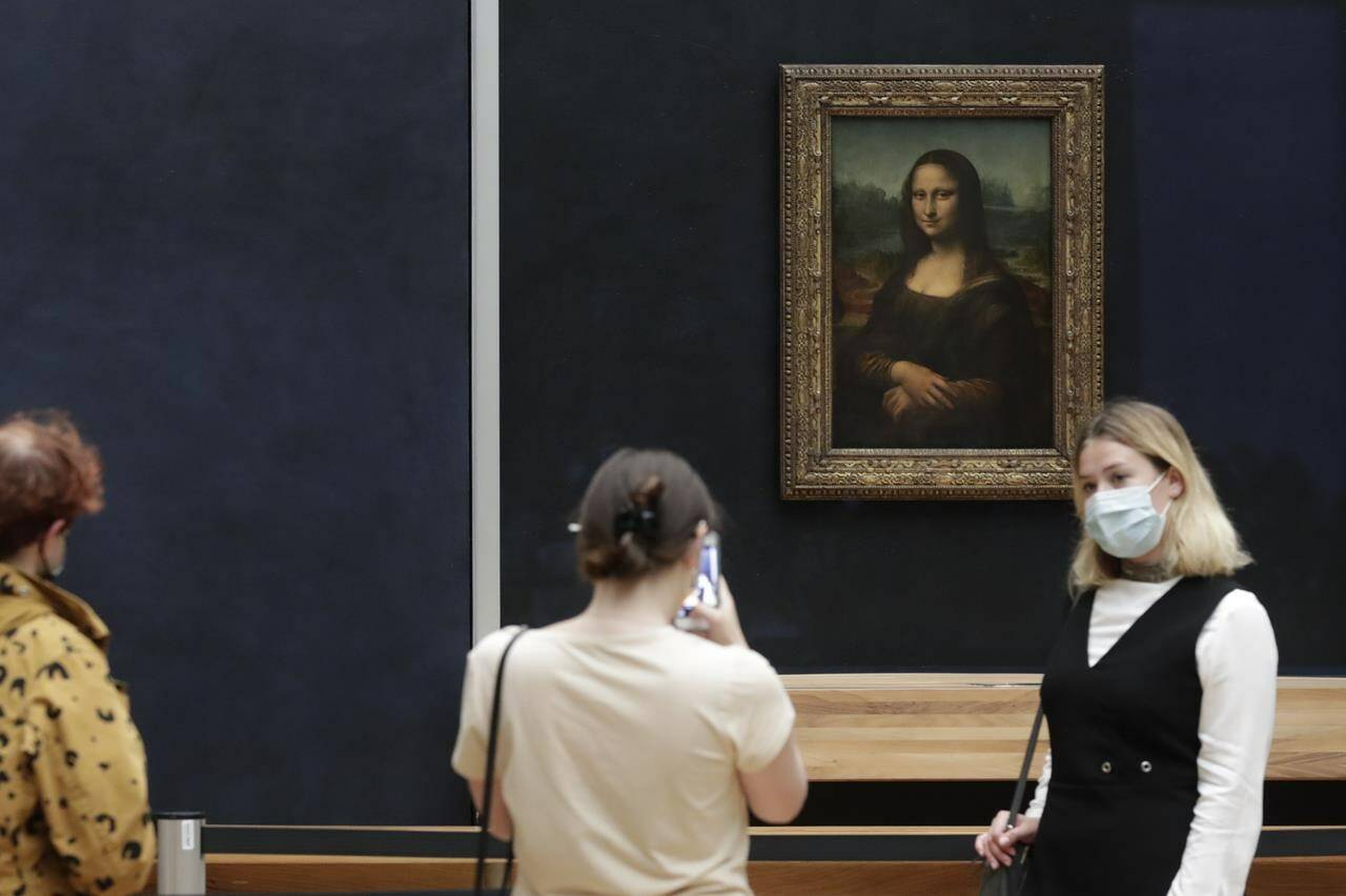 FILE - Visitors pose in front of Leonardo da Vinci's Mona Lisa in the Louvre museum, Wednesday, May, 19, 2021 in Paris. A man seemingly disguised as an old woman in a wheelchair threw a piece of cake at the glass protecting the Mona Lisa on Sunday May 29, 2022 at the Louvre Museum and shouted at people to think of planet Earth. (AP Photo/Thibault Camus, File)