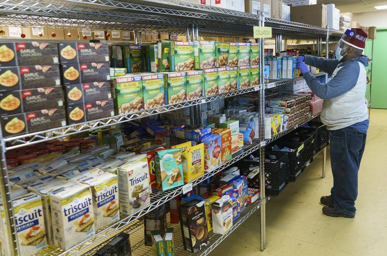 A worker fills the shelves at a food bank in Montreal, on Wednesday, January 27, 2021. A new survey suggests a growing number of Canadians are struggling with the rising cost of food as prices for basics like pasta, bread and meat all soar. THE CANADIAN PRESS/Paul Chiasson