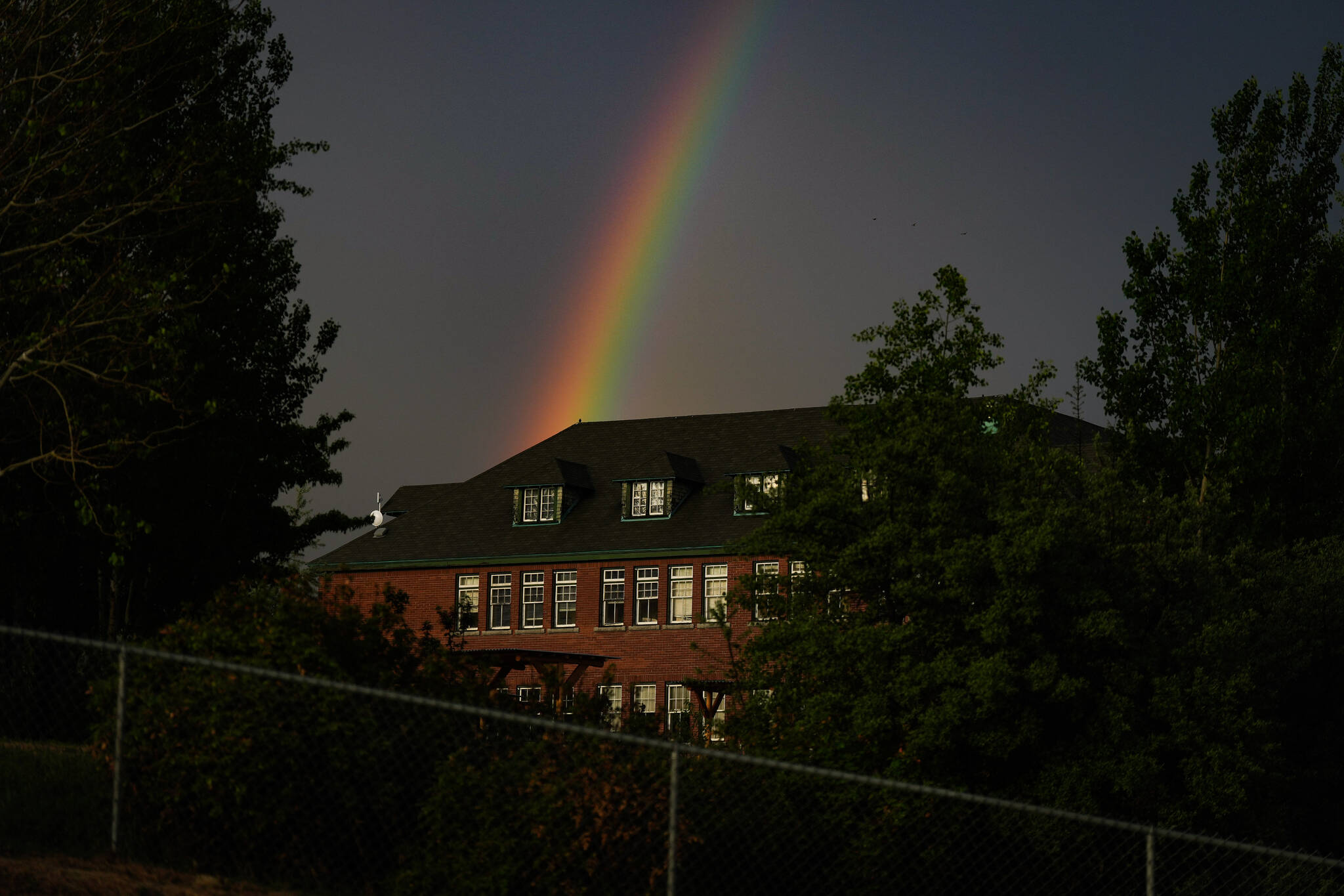 A rainbow is seen in the distance behind the former Kamloops Indian Residential School after a day-long ceremony to mark the one-year anniversary of the Tk’emlups te Secwepemc announcement of the detection of the remains of 215 children at an unmarked burial site at the former residential school, in Kamloops, B.C., on Monday, May 23, 2022. THE CANADIAN PRESS/Darryl Dyck