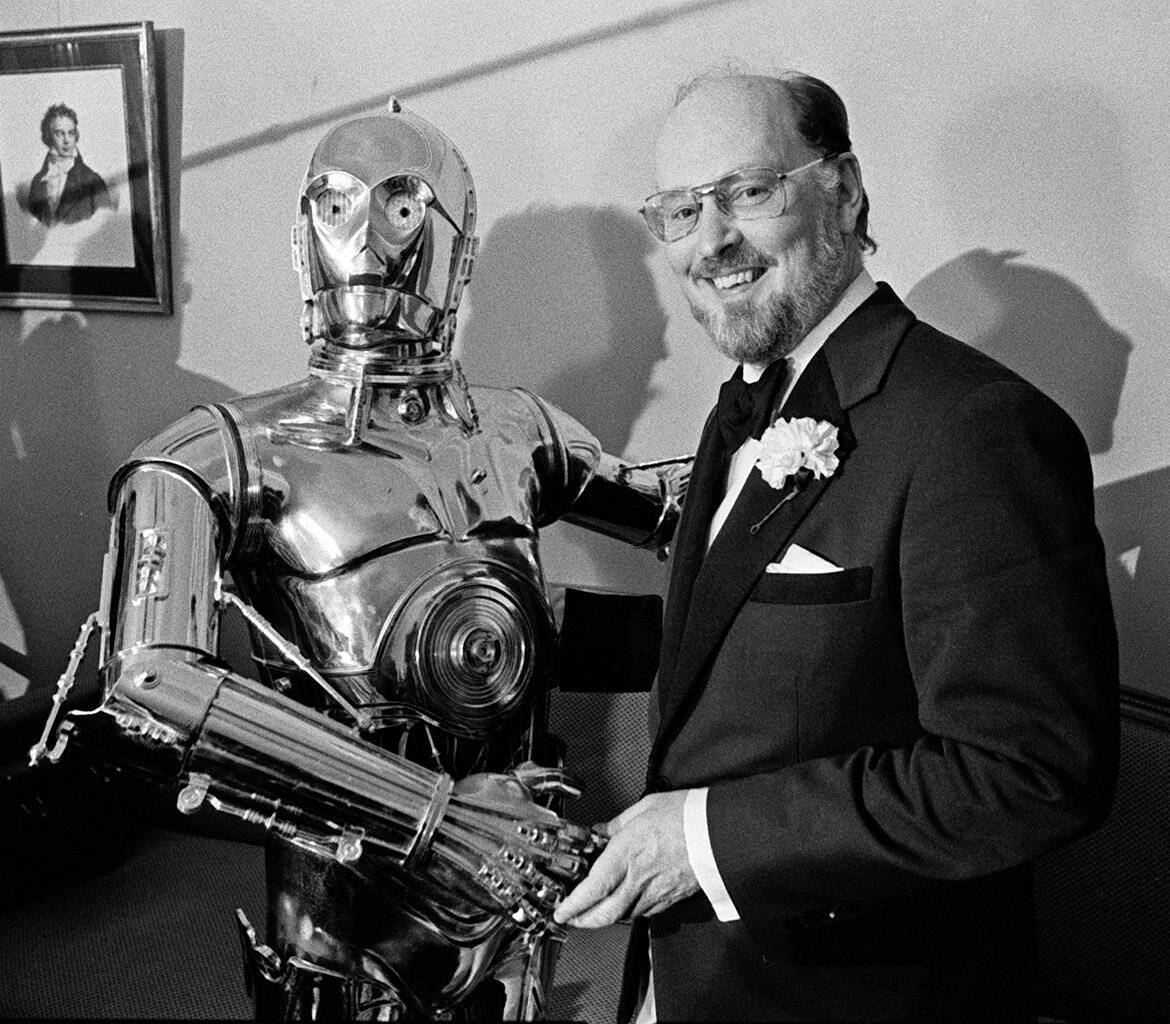 FILE - Boston Pops conductor John Williams, right, shakes hands with “Star Wars” character C-3PO at a news conference in Boston on April 30, 1980. Williams, 90, is devoting himself to composing concert music, including a piano concerto he’s writing for Emanuel X. This spring, he and cellist Yo-Yo Ma released the album “A Gathering of Friends,” recorded with the New York Philharmonic.(AP Photo, File)