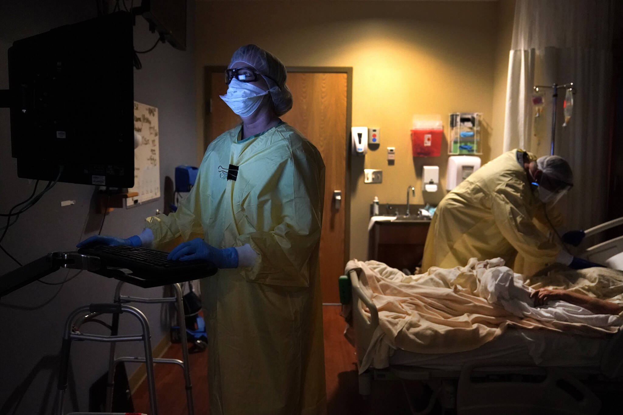 FILE - Registered nurse Shelly Girardin, left, is illuminated by the glow of a computer monitor as Dr. Shane Wilson examines COVID-19 patient Neva Azinger. (AP Photo/Jeff Roberson, File)