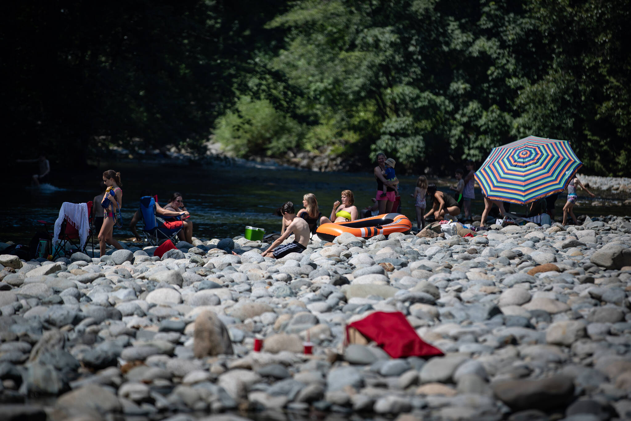 People sit on rocks while cooling off in the frigid Lynn Creek water in North Vancouver, B.C., on Monday, June 28, 2021. THE CANADIAN PRESS/Darryl Dyck