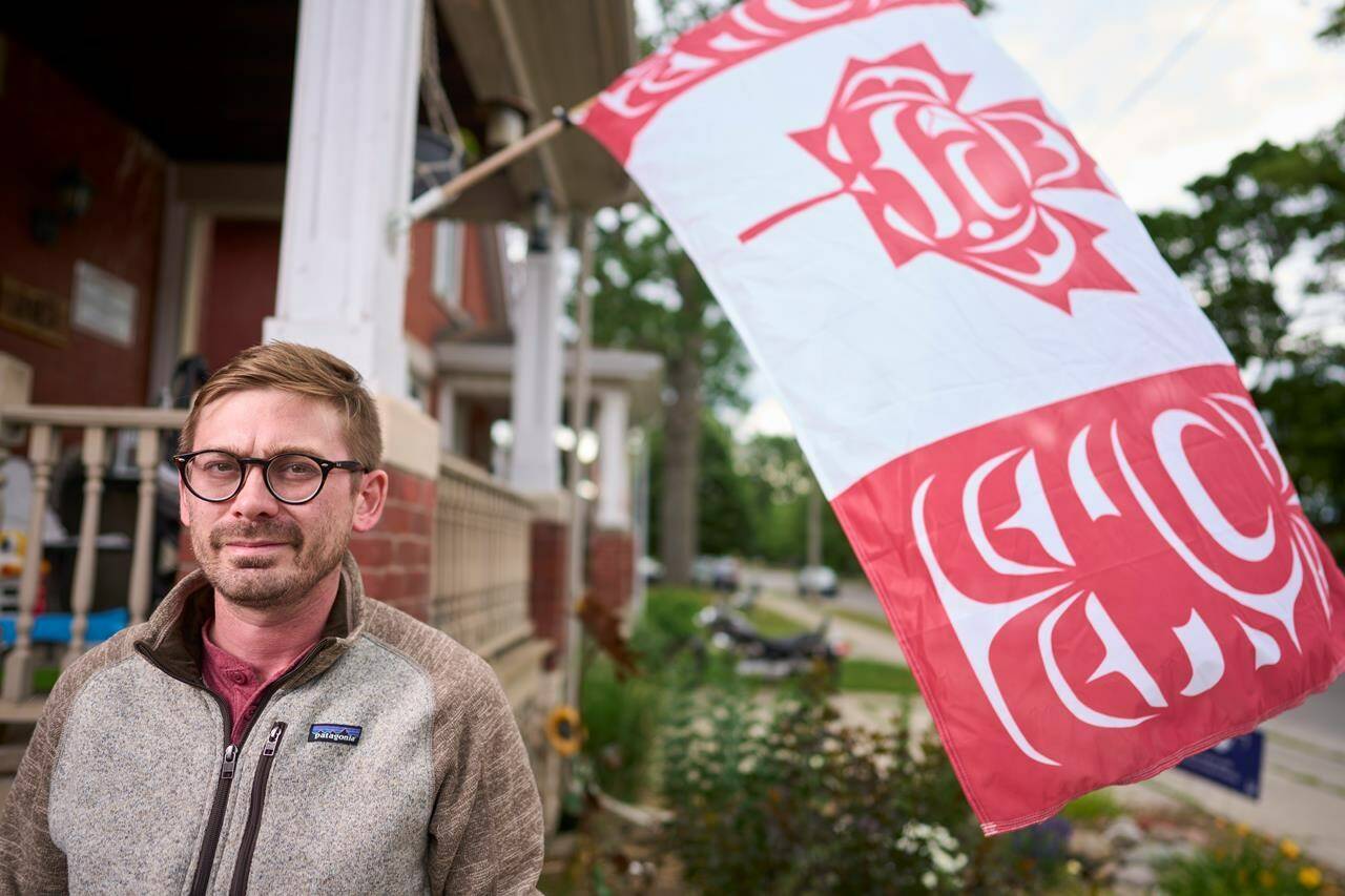 Blaine Chalk poses for a photo in front of his home in London, Ont., where he flies a version of the Canadian Flag designed by Indigenous artist Curtis Wilson, Monday, June 27, 2022. THE CANADIAN PRESS/Geoff Robins