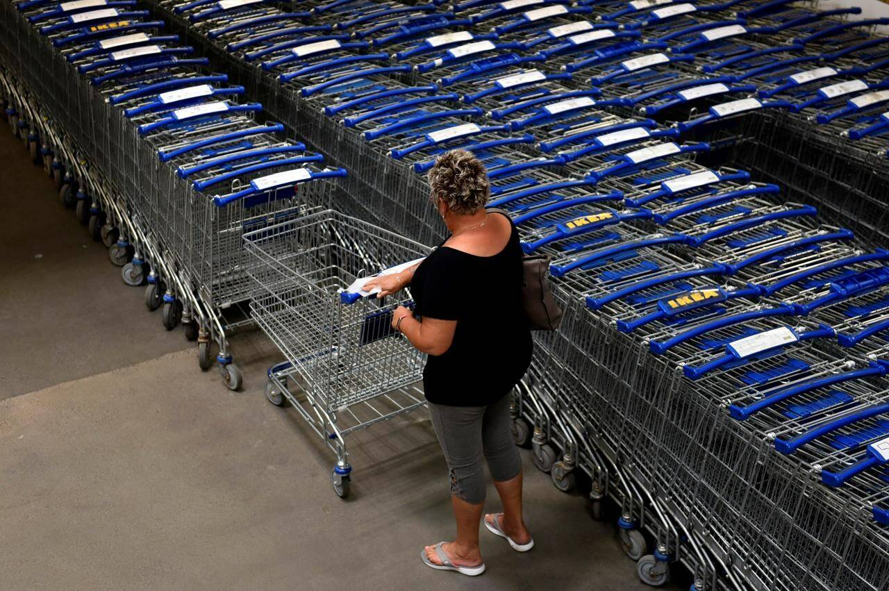 A shopper wipes down a handle as they select a cart at an Ikea furniture store in Ottawa, Tuesday, May 31, 2022. Canadian retailers are struggling with higher shipping costs as couriers tack hefty fuel surcharges onto shipping rates to recoup record gas prices. THE CANADIAN PRESS/Justin Tang