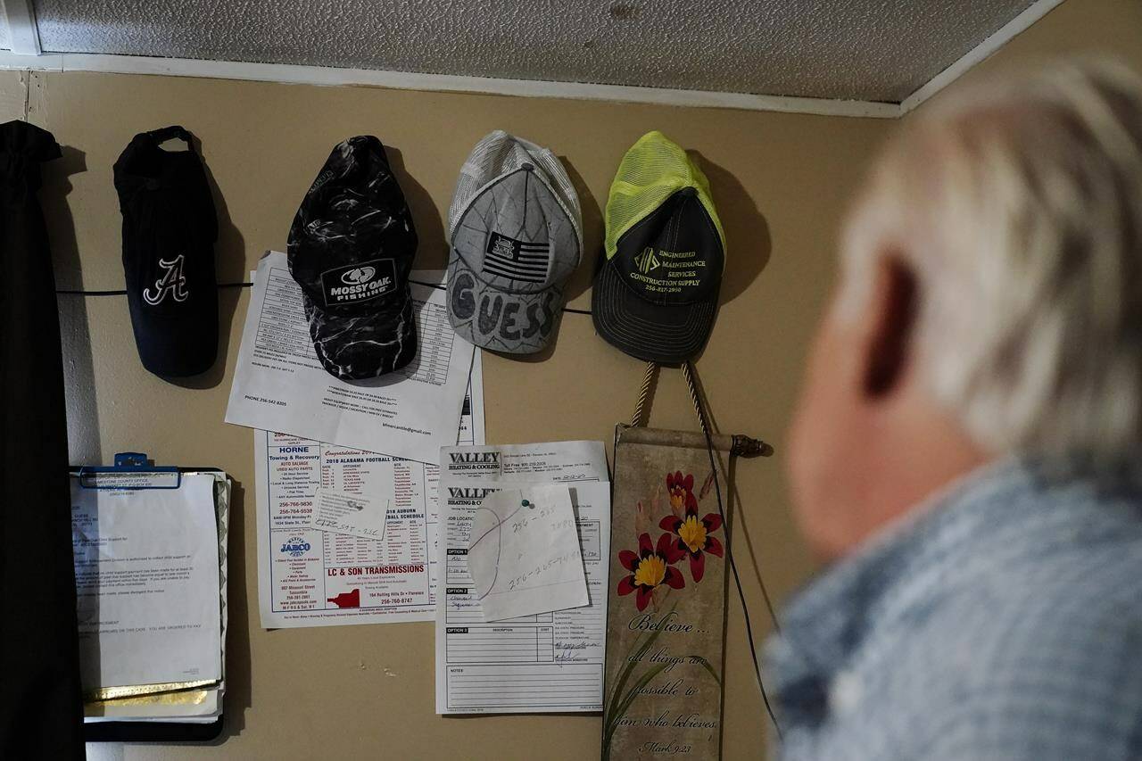 Larry Guess looks at a line of hats on his bedroom wall, one that says Guess on the brim belonged to his son, his son, David Guess, Thursday, June 23, 2022, in Athens, Ala. David Guess, 51, was killed by gun violence in March. His killing drew little attention outside the rural stretch of northern Alabama where Guess grew up and later worked as a mechanic and truck driver, though his death shattered many lives. (AP Photo/Brynn Anderson)