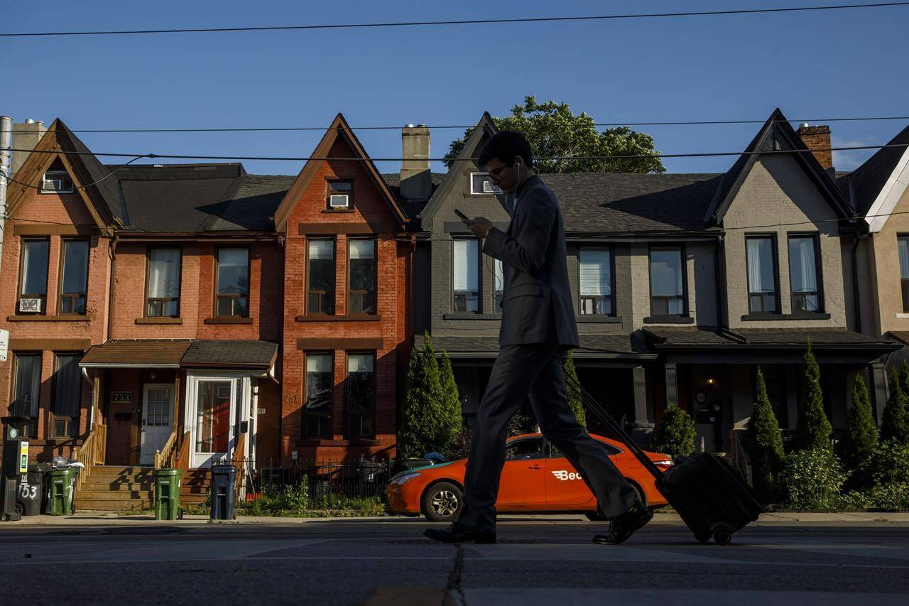 A person walks by a row of houses in Toronto on Tuesday July 12, 2022. Multigenerations living under one roof is becoming increasingly common, Statistics Canada’s latest tranche of census data revealed Wednesday.THE CANADIAN PRESS/Cole Burston