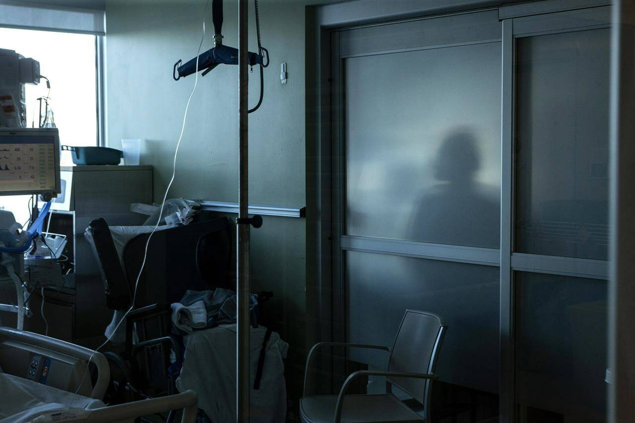 A nurse is silhouetted behind a glass panel as she tends to a patient in the intensive care unit at the Bluewater Health Hospital in Sarnia, Ont., on Tuesday, Jan. 25, 2022. THE CANADIAN PRESS/Chris Young