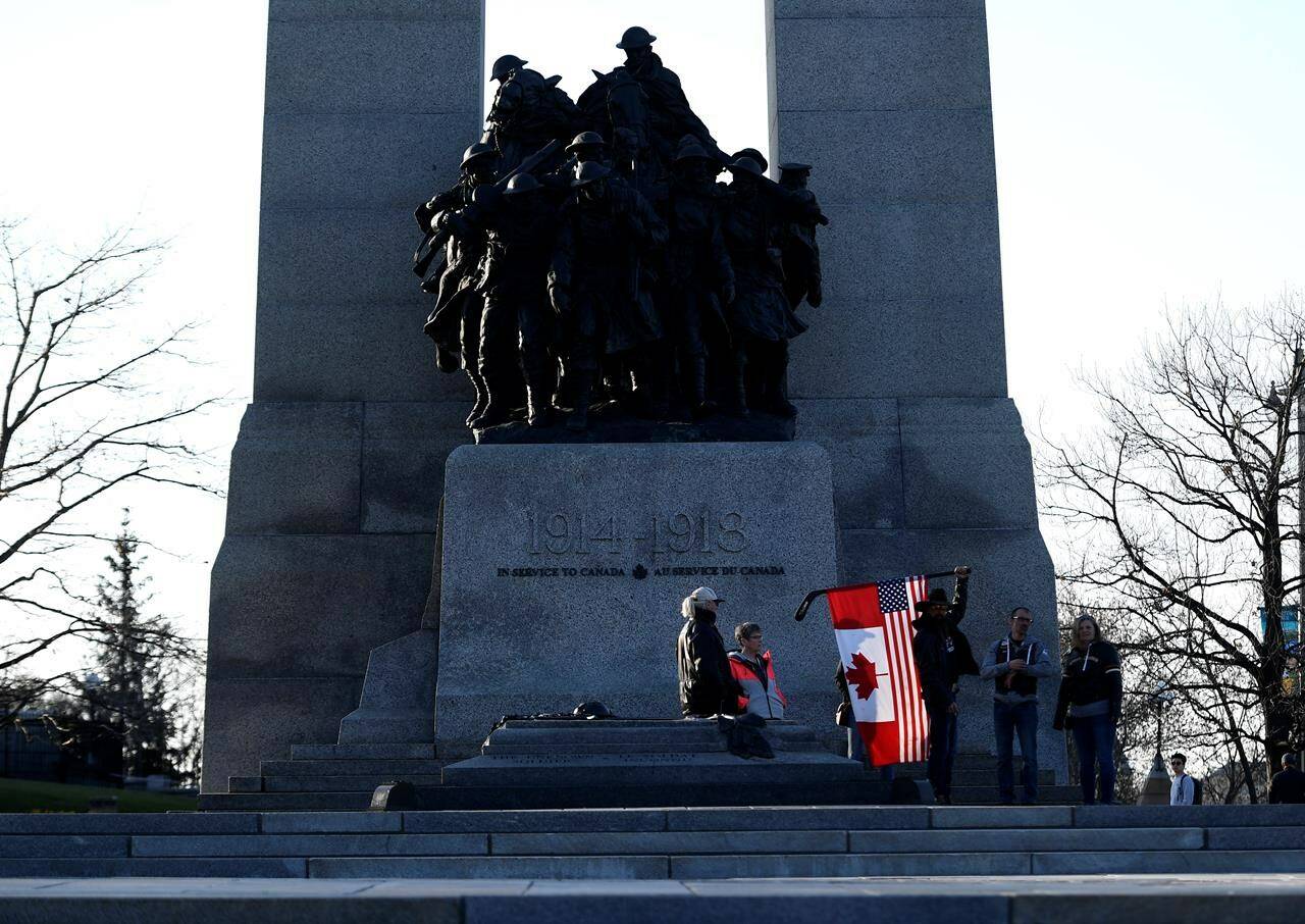 A person holds a combination American and Canadian flag at the Tomb of the Unknown Soldier at the National War Memorial before a march at a demonstration, part of a convoy-style protest participants are calling “Rolling Thunder”, in Ottawa, on Friday, April 29, 2022. THE CANADIAN PRESS/Justin Tang