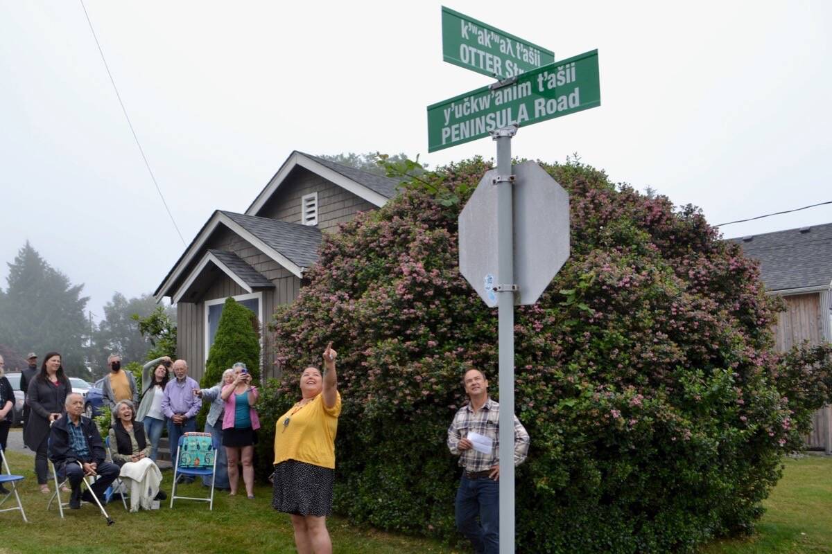 Jeneva Touchie points to a new bilingual Nuu-chah-nulth / English street sign across from the high school. The District of Ucluelet hosted a small gathering on July 29 to unveil the new bilingual sign, which will be one of many installed around town over the next few months. (Nora O’Malley photo)