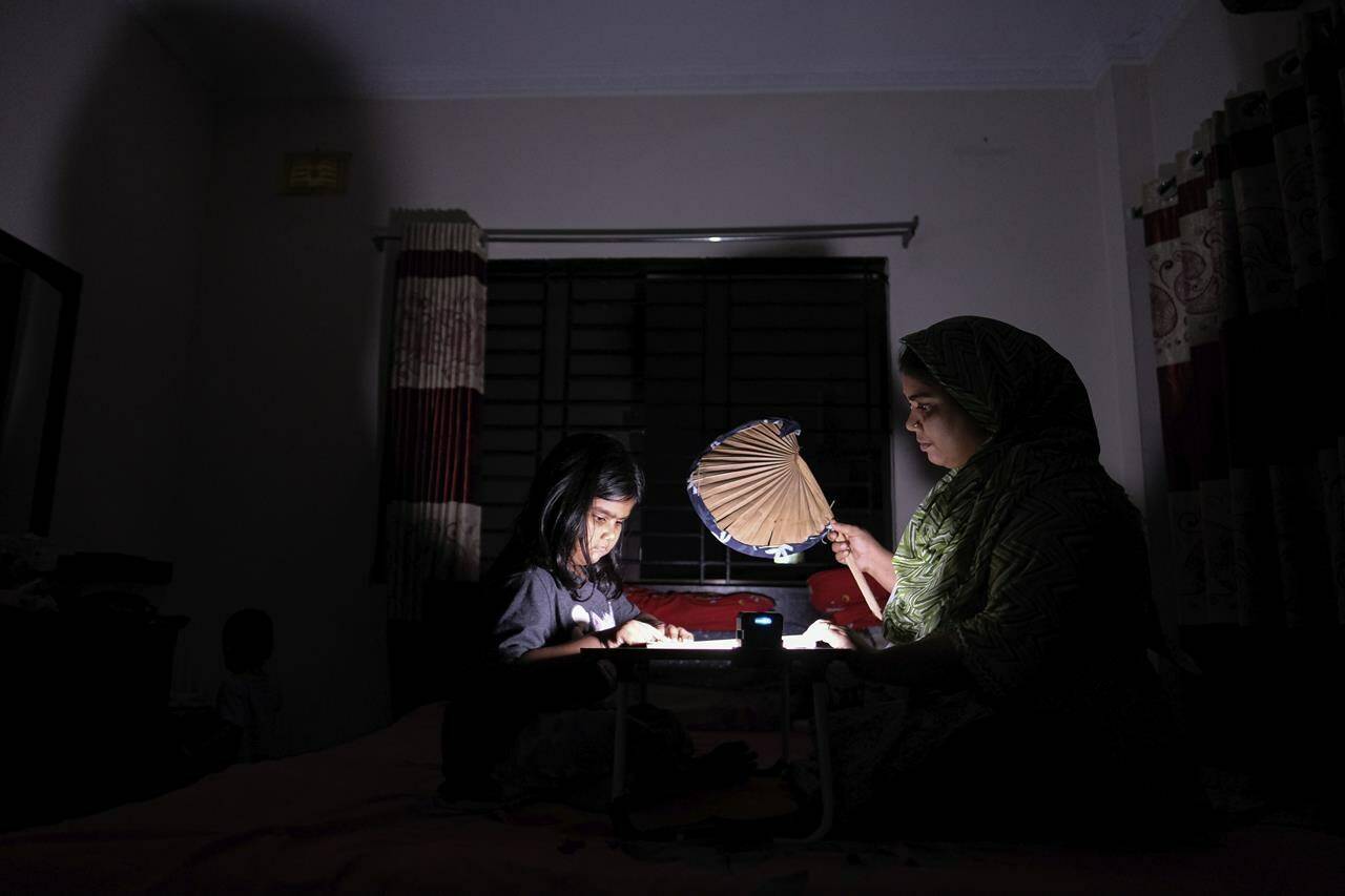 A Bangladeshi woman uses a traditional hand fan as she assists her daughter in her studies during a power cut at their home in Pilkhana area, Dhaka, Bangladesh, Tuesday, Aug.23, 2022. Schools in Bangladesh will close an additional day each week and government offices and banks will shorten their work days by an hour to reduce electricity usage amid concerns over rising fuel prices and the impact of the Ukraine war. (AP Photo/Mahmud Hossain Opu)