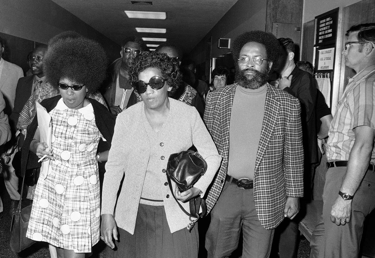 FILE - Georgia Jackson, center, accompanied by the Rev. Cecil Williams, right, of Glide Memorial Church in San Francisco, arrive at the Hall of Justice on Aug. 24, 1971, for a court appearance of two surviving Soledad Brothers - John Clutchette and Fleeta Drumgo. Jackson’s son, George Jackson, was killed on Saturday, Aug. 21, 1971, at San Quentin prison. First celebrated in 1979, Black August was originally created to commemorate Jackson’s fight for Black liberation. Fifty one years since his death, Black August is now a month-long awareness campaign and celebration dedicated to Black American freedom fighters, revolutionaries, radicals and political prisoners, both living and deceased. (AP Photo/Richard Drew, File)