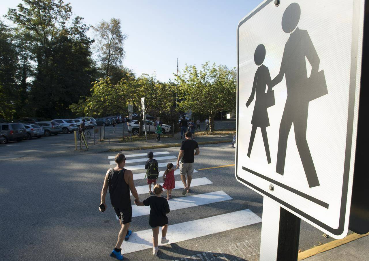 Children walk with their parents to Sherwood Park Elementary in North Vancouver for their first day back to school on Sept. 10, 2020. Masks remain optional in newly released British Columbia guidelines for schools, but some teacher and parent groups are seeking more stringent COVID-19 protocols. THE CANADIAN PRESS/Jonathan Hayward