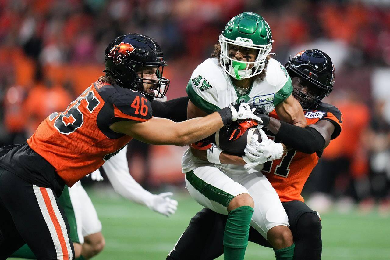 B.C. Lions' Ben Hladik, left, and Jordan Williams, back right, tackle Saskatchewan Roughriders' Kian Schaffer-Baker during the first half of CFL football game action in Vancouver on Friday, Aug. 26, 2022. THE CANADIAN PRESS/Darryl Dyck