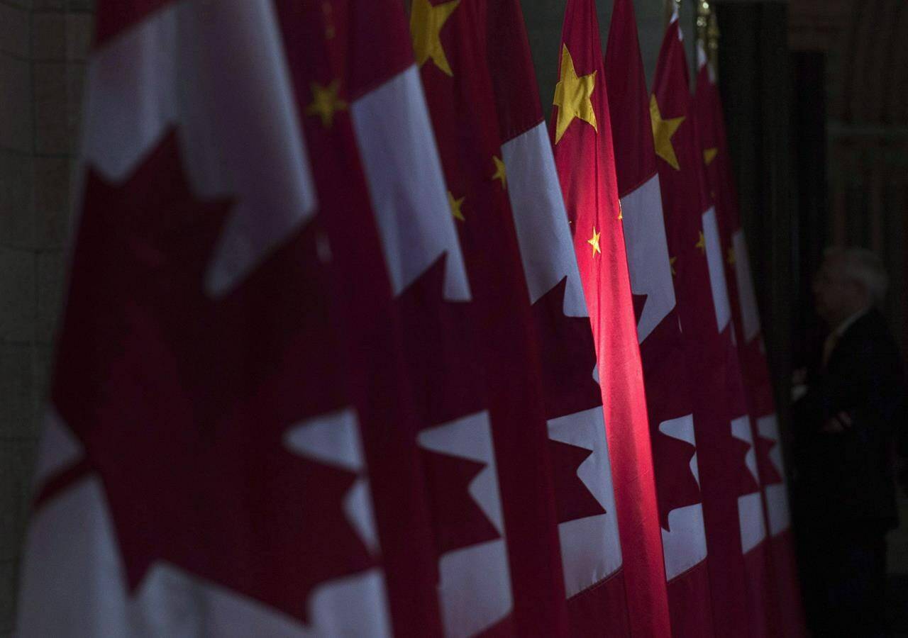 A Chinese flag, flanked by Canadian flags, is illuminated by sunshine in the Hall of Honour on Parliament Hill in Ottawa, on Sept. 22, 2016. THE CANADIAN PRESS/Adrian Wyld