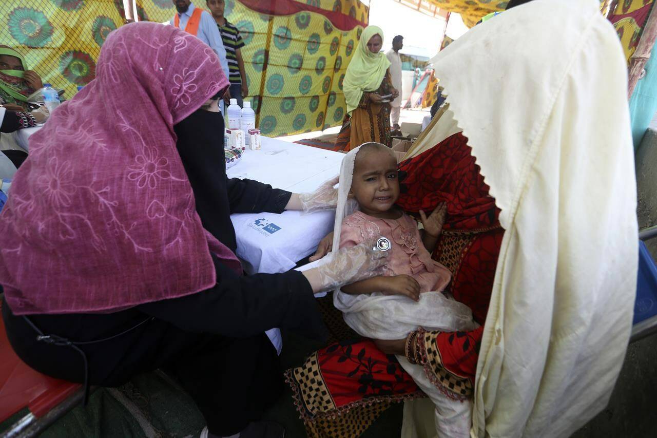 A doctor checks on a sick girl in the clinic organized by Islamic group Jamaat-e-Islami Pakistan, after her home was hit by floods in Sukkur, Pakistan, Sunday, Sept. 4, 2022. Officials warned Sunday that more flooding was expected as Lake Manchar in southern Pakistan swelled from monsoon rains that began in mid-June and have killed nearly 1,300 people. (AP Photo/Fareed Khan)