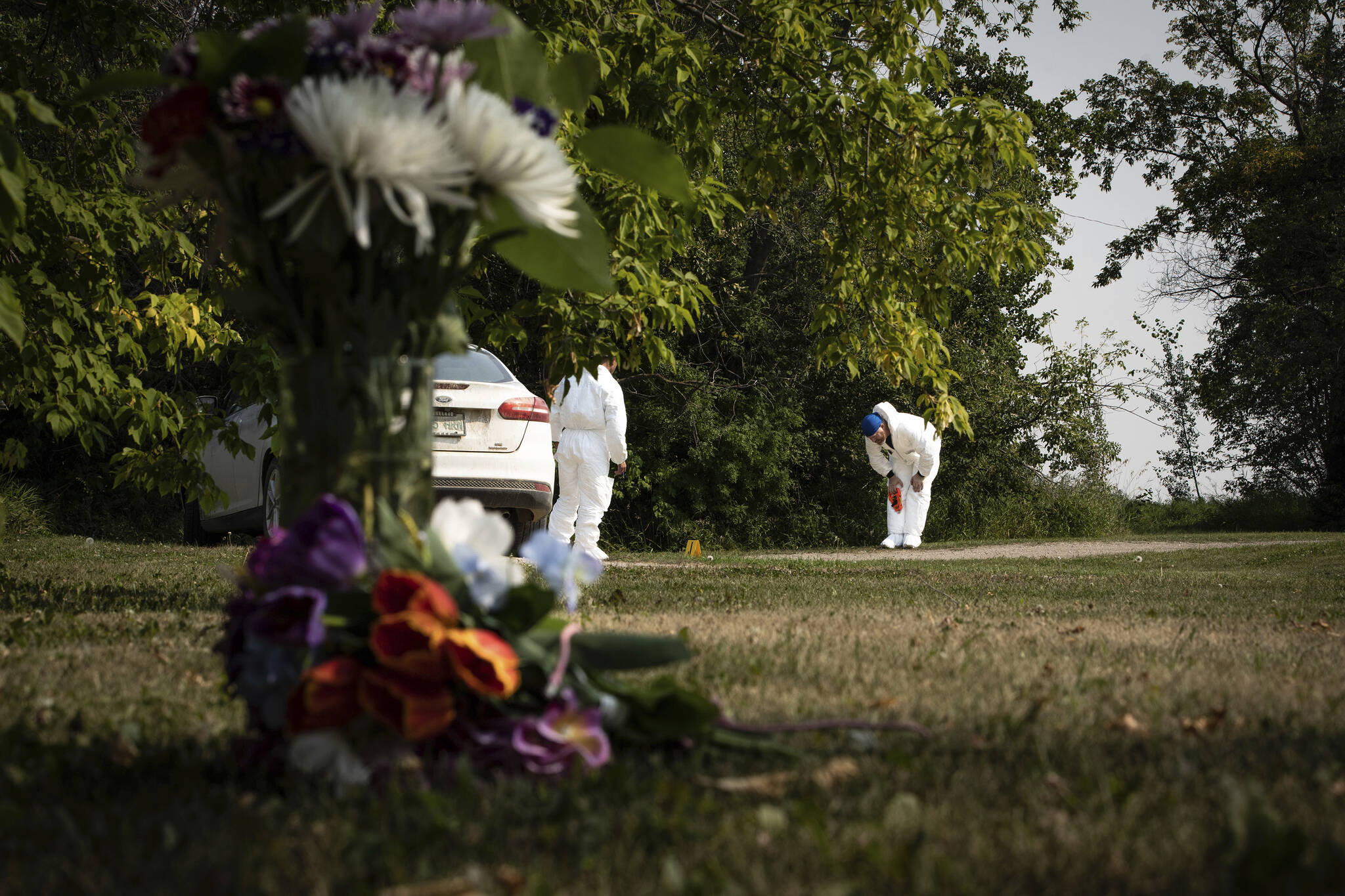 Investigators examine the crime scene near a memorial of flowers outside the home of Wes Petterson in Weldon, Saskatchewan, Monday, Sept. 5, 2022. Petterson, 77, was killed in a series of stabbings in the area on Sunday. (AP Photo/Robert Bumsted)