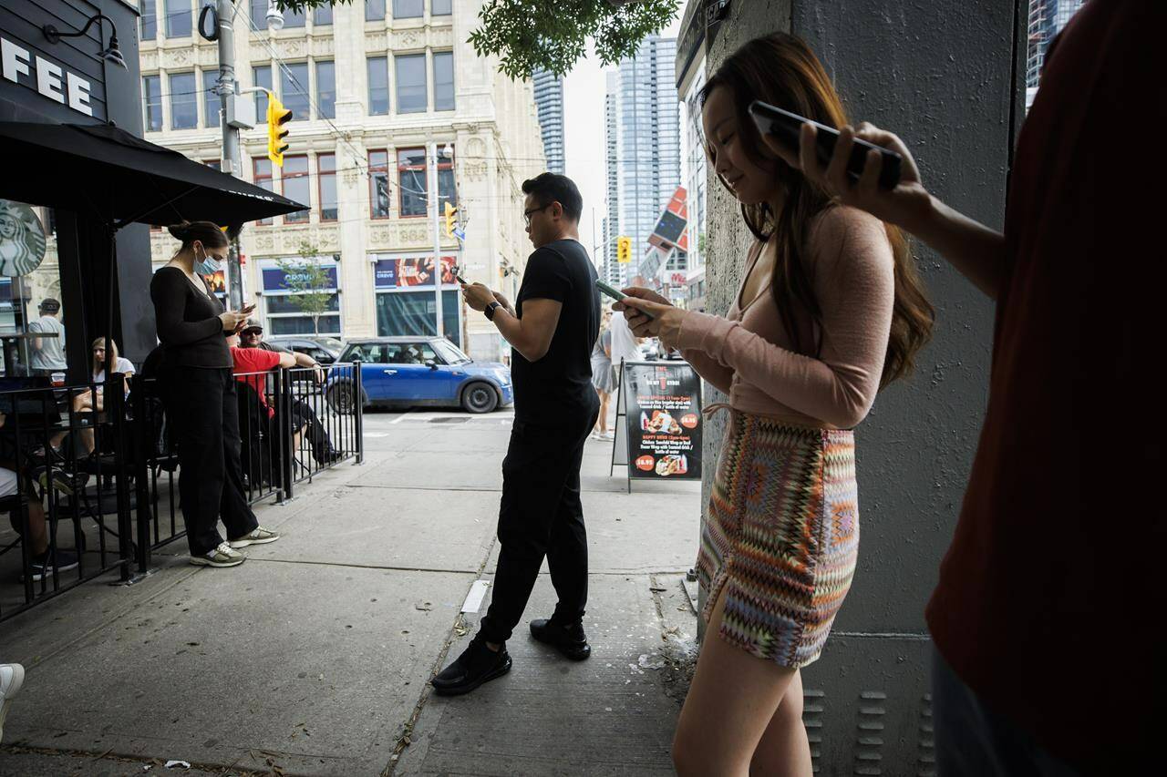 People use electronics outside a coffee shop in Toronto amid a nationwide Rogers outage, affecting many of the telecommunication company’s services, Friday, July 8, 2022. THE CANADIAN PRESS/Cole Burston