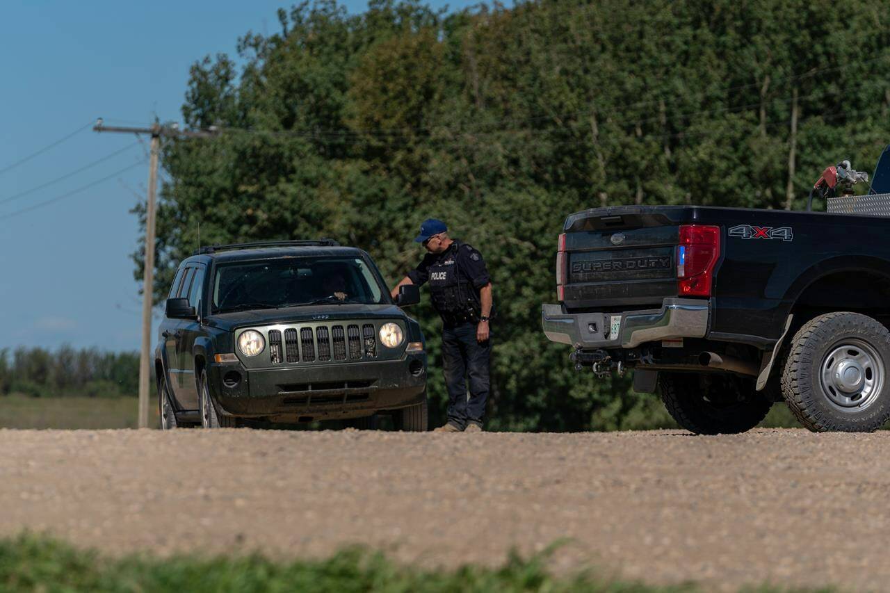 An RCMP officer interacts with a driver at a police roadblock in James Smith Cree Nation, Sask., on Tuesday, September 6, 2022. A manhunt for the fugitive suspect in the Saskatchewan mass killing continues today after a tense police search yesterday came up empty. THE CANADIAN PRESS/Heywood Yu