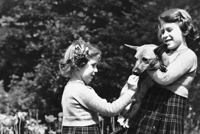 FILE - In this July 5, 1936 file photo, Britain’s Princess Elizabeth, right, holds a Pembrokeshire Corgi as her sister Princess Margaret feeds it a biscuit. Queen Elizabeth II, Britain’s longest-reigning monarch and a rock of stability across much of a turbulent century, has died. She was 96. Buckingham Palace made the announcement in a statement on Thursday Sept. 8, 2022. (AP Photo, File)
