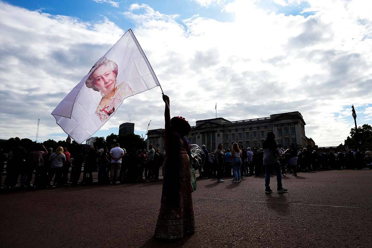 A women waves a flag with a photograph of the late Queen Elizabeth II as thousands of people mourn as pay their respects at the gates of Buckingham Palace in London, Saturday, Sept. 10, 2022. Queen Elizabeth II, Britain’s longest-reigning monarch and a rock of stability across much of a turbulent century, died Thursday Sept. 8, 2022, after 70 years on the throne. She was 96. THE CANADIAN PRESS/Nathan Denette