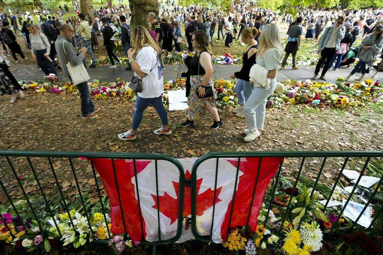 Long lines of mourners form and lay flowers near a Canadian flag as people wait to pay their respect near the gates of Buckingham Palace in London on Sunday, September 11, 2022. Queen Elizabeth II, Britain’s longest-reigning monarch and a rock of stability across much of a turbulent century, died Thursday Sept. 8, 2022, after 70 years on the throne. She was 96. THE CANADIAN PRESS/Nathan Denette