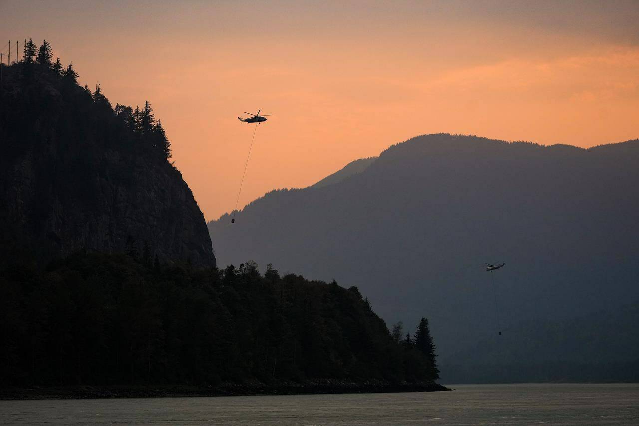 Helicopters with water buckets battling the Flood Falls Trail wildfire pick up water from the Fraser River, in Hope, B.C., Monday, Sept. 12, 2022. THE CANADIAN PRESS/Darryl Dyck