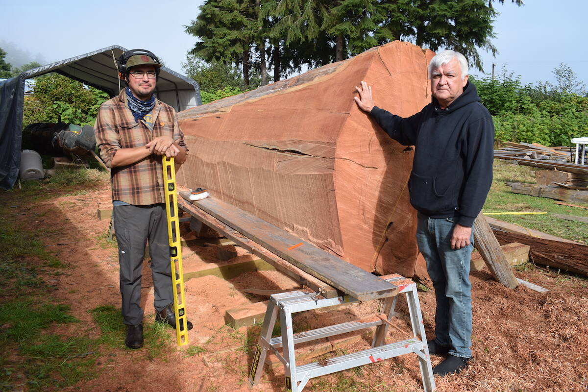 Apprentice carver Rey Dickie and master carver Stan Hunt stand next to the log that will be carved into a monument to remember Indigenous children who died at residential schools. (Tyson Whitney - North Island Gazette)