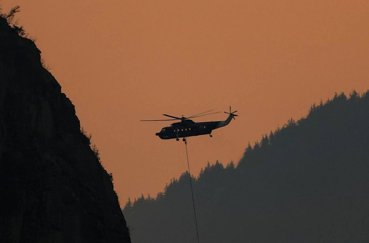 A helicopter with a water bucket battling the Flood Falls Trail wildfire picks up water from the Fraser River, in Hope, B.C., Monday, Sept. 12, 2022. Cool, showery weather is helping wildfire crews make progress on the five highly visible or potentially damaging wildfires currently burning in British Columbia. THE CANADIAN PRESS/Darryl Dyck